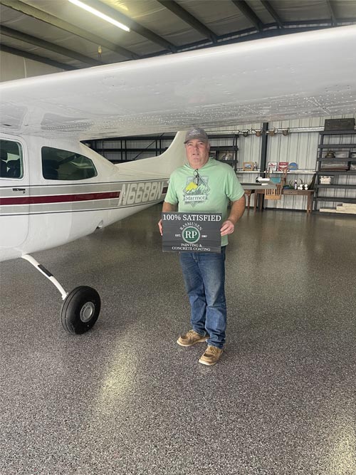 Man holding 100% satisfied sign by an airplane