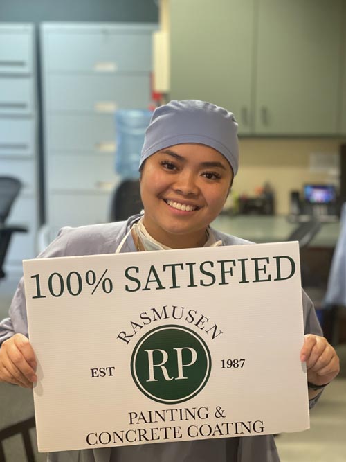 Person holding 100% satisfied sign while in medical scrubs